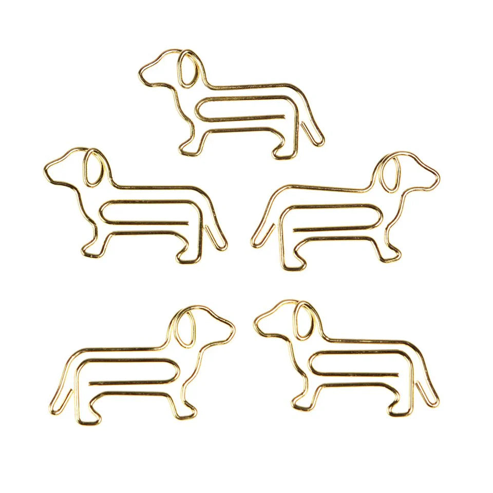 Five gold dog-shaped paper clips from rex london on a white background