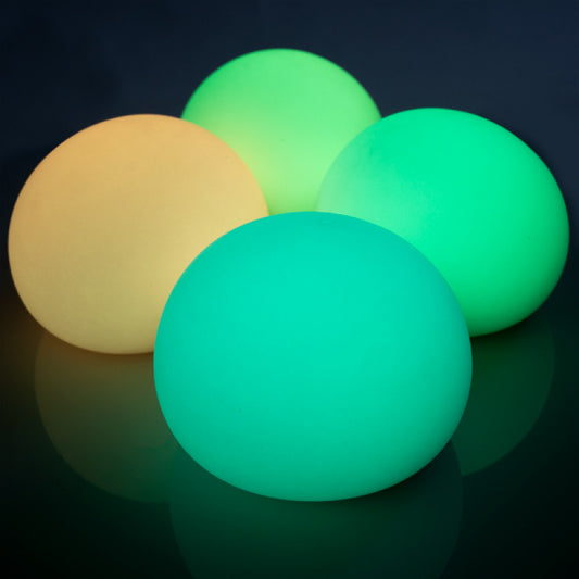 Four Smooshos Jumbo Glow in the Dark Ball glowing balls in yellow, green, and teal on a reflective surface with a dark background