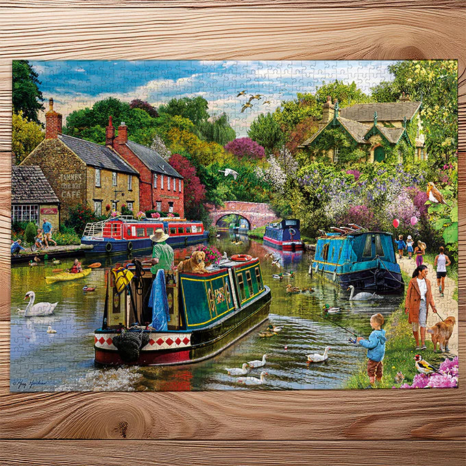 Colorful jigsaw puzzle of a canal scene with boats, people, and ducks on a wooden surface.