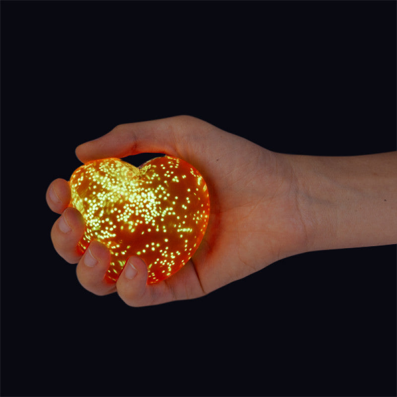 Hand holding a Smooshos Super Squeeze Glow in the Dark Heart against a black background