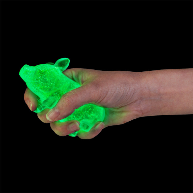 Hand holding a Smooshos Super Squeeze Glow in the Dark Pig against a black background