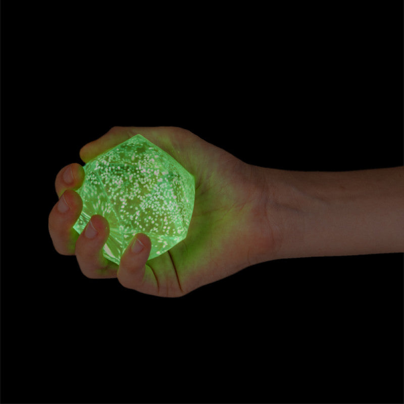 Hand holding a Smooshos Super Squeeze Glow in the Dark Polyhedron against a black background