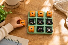 A child's hand holding a small green tic-tac-toe board with wooden wombat and Tasmanian devil pieces.